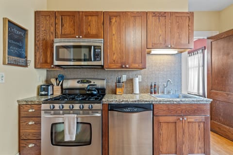 A compact kitchen featuring wooden cabinetry, a stainless steel stove, and modern appliances.