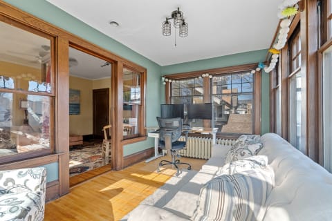 A bright home office featuring a white couch, two computer monitors, and colorful string lights.