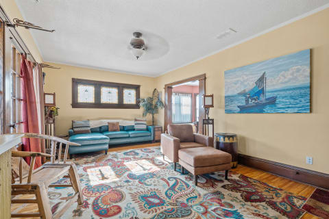 A living room with a turquoise sectional sofa, stained glass windows, and a nautical painting.