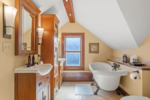 Vintage bathroom with vaulted ceiling, wooden cabinets, sinks, and a freestanding bathtub.