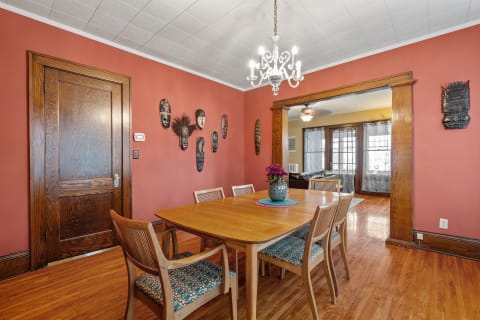 A cozy dining room with a wooden table, colorful chair cushions, and tribal masks on the wall.