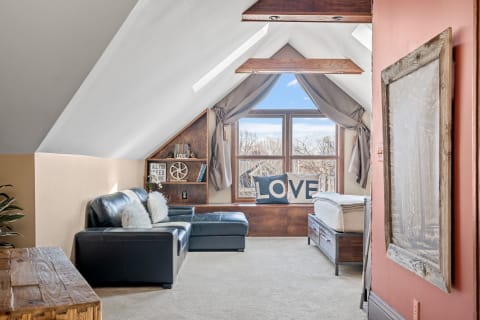 Bright attic room with a black leather sofa, large window, and decorative elements.