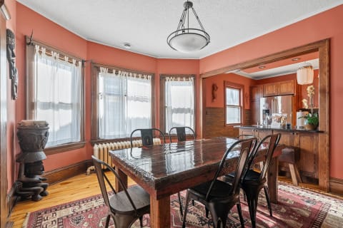 Dining room featuring a wooden table, black chairs, terracotta walls, and large windows.