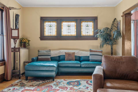 A living room with a teal sectional sofa, decorative cushions, stained glass windows, and sunflowers.