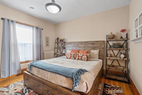 Cozy bedroom featuring a wooden bed, decorative pillows, shelves with decor, and sheer curtains.
