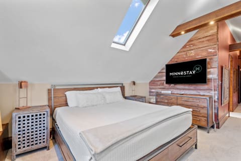 A cozy bedroom featuring a queen-sized bed, wooden furniture, and a skylight.
