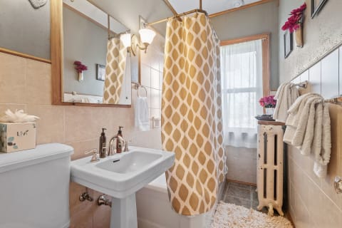 Cozy bathroom with a patterned shower curtain, a mirror, and floral decorations.