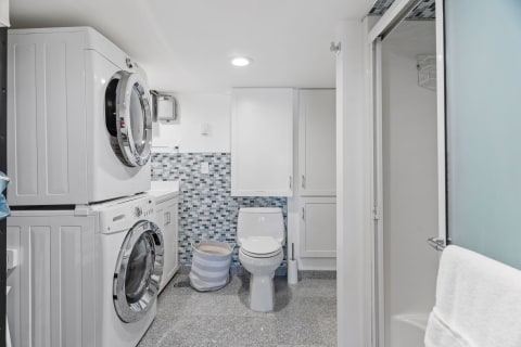 Interior view of a contemporary laundry and bathroom area with stacked washer and dryer, toilet, and shower.