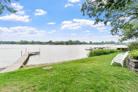 A peaceful lakeside scene featuring a wooden dock, boats, and green grass.