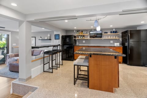 A contemporary kitchen featuring a granite island, bar stools, and a cozy couch with shelves above.