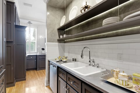 Stylish kitchen with dark cabinetry, farmhouse sink, and open shelving displaying dinnerware.