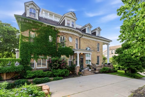 Historic brick house with ivy-covered walls, elegant columns, and lush gardens on a private driveway.