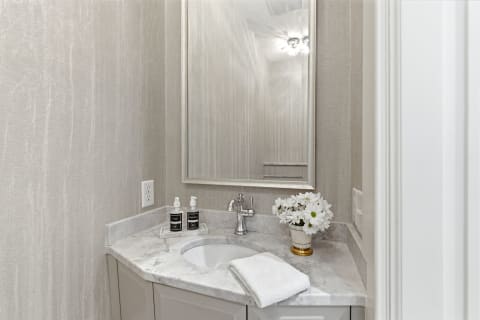 Elegant private bathroom with marble countertop, a round sink, soap dispensers, and fresh flowers.