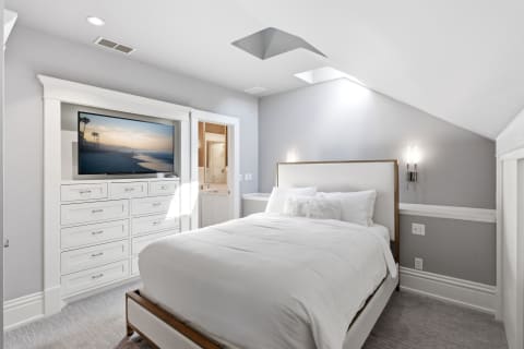 A modern coastal bedroom with white bedding, a mounted TV, and soft ambient lighting.