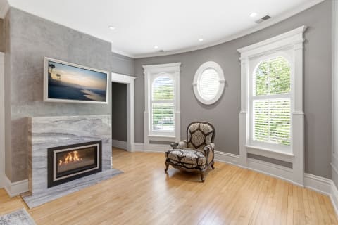 Cozy corner with an ornate armchair, marble fireplace, and large windows letting in natural light.