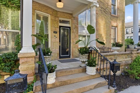 An entrance to a brick townhouse framed by white columns and tropical plants.