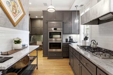 Modern kitchen featuring gray cabinetry, marble countertops, and stainless steel appliances beneath a warm glow of natural light.