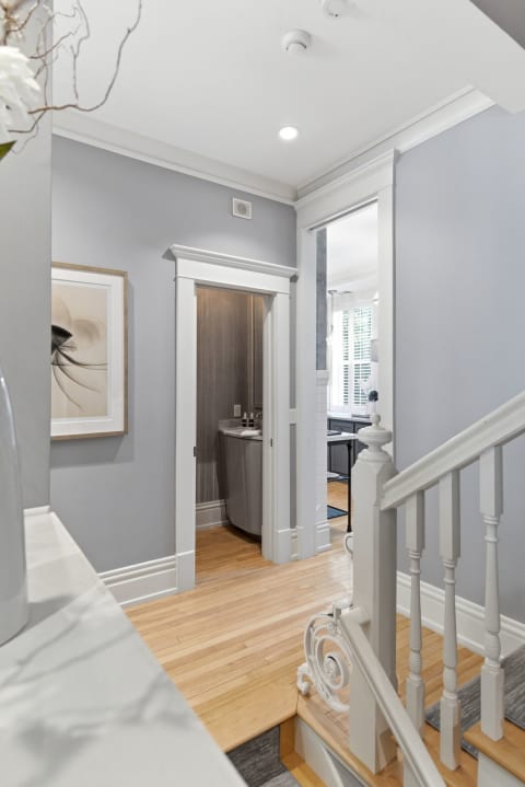 A stylish hallway with gray walls, hardwood floors, framed art, and a staircase leading upwards.