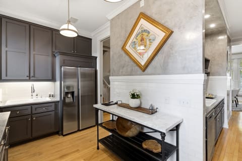 Sophisticated kitchen with dark cabinetry, stainless-steel appliances, and a marble island, featuring artwork on the wall.