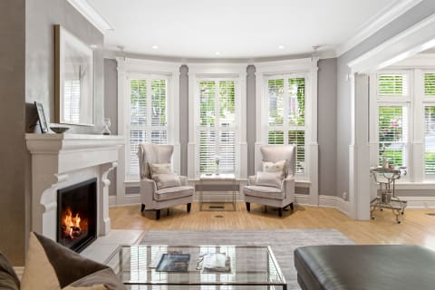 A comfortable living room with plush armchairs, a fireplace, and large windows adorned with shutters.