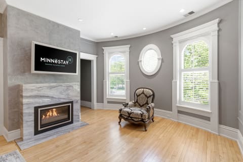 A living room with a fireplace, ornate armchair, and elegant design details including round and arched windows.