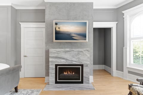 A chic living room featuring a marble fireplace, a coastal artwork, and warm hardwood floors.