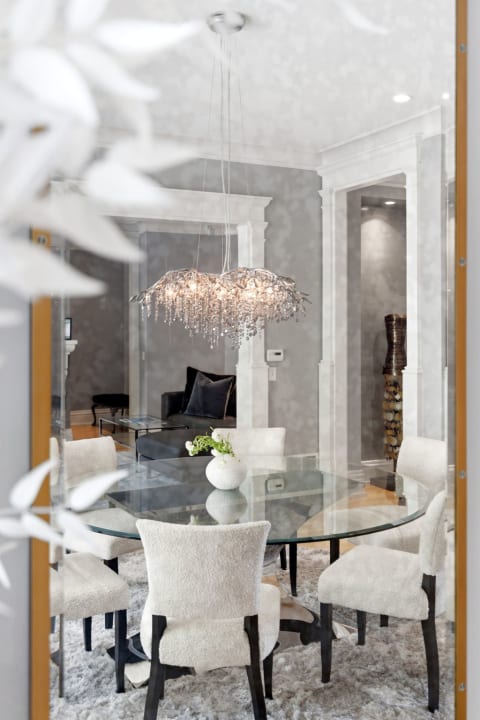 A modern dining space with a crystal chandelier above a glass table surrounded by cushioned chairs.