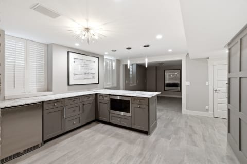 A modern kitchen with sleek marble counters, gray cabinets, and elegant lighting fixtures.