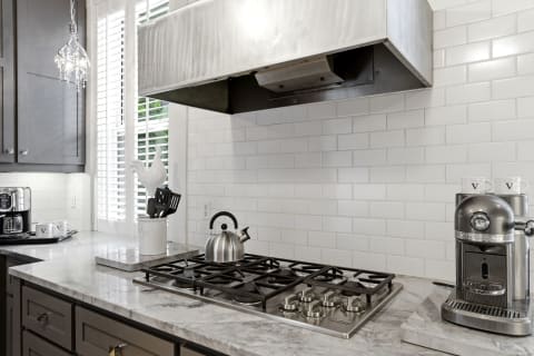 A stylish kitchen with marble countertops, a gas stove, and stainless steel appliances, complemented by a unique white ceramic decoration.