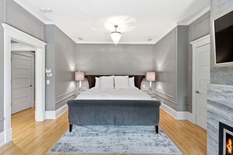 A serene bedroom with a plush gray bed, warm hardwood flooring, and elegant decor.