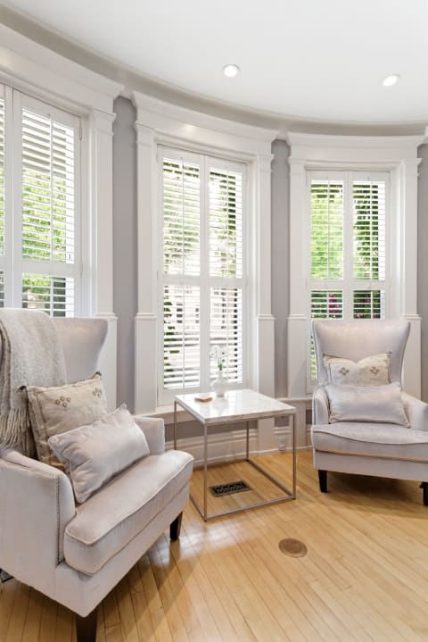 Elegant sitting nook with wingback chairs, a marble table, and natural light filtering through shutters.