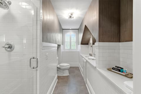 A luxurious bathroom with white tiles, wood cabinetry, and a well-organized countertop.
