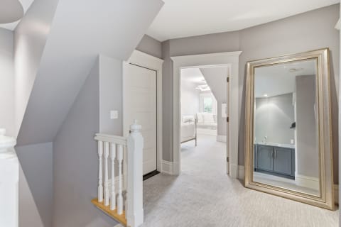 An elegant upstairs hallway featuring soft gray walls, a plush carpet, and a gold-framed mirror, leading to a cozy room.