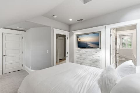 A serene bedroom suite with a white bed, wall-mounted TV, and adjoining bathroom.