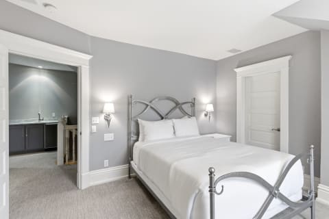Plush queen bed in a serene gray-walled bedroom with a doorway leading to an en-suite.