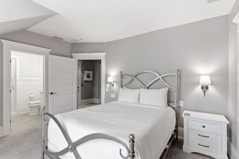 A cozy bedroom with a gray wall, white linens on a silver bed frame, and soft lighting from wall sconces.