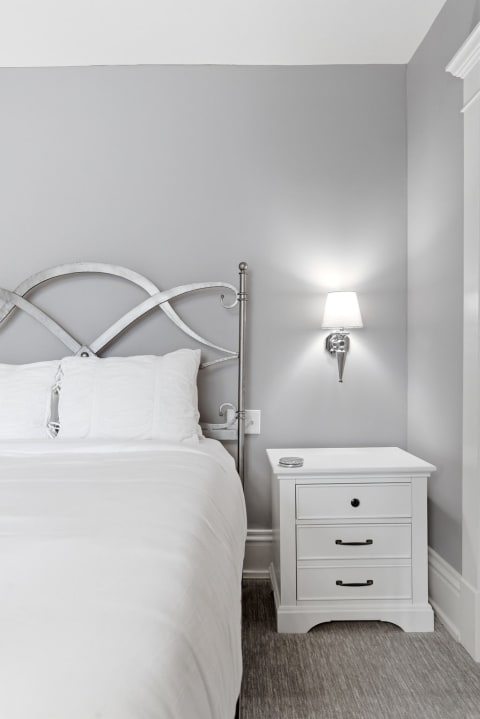 A serene bedroom featuring a metallic headboard, white linens, and a stylish nightstand illuminated by a warm bedside lamp.