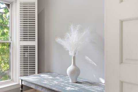 A weathered gray bench with a white vase holding delicate white plumes, lit by sunlight.