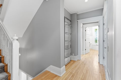 Light-filled hallway with hardwood floors and towel shelving leading to a private area.