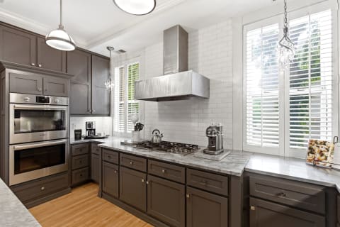 A modern kitchen with dark cabinets, marble countertops, and stainless steel appliances, highlighted by natural light from windows.