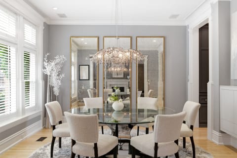 Elegant dining area with a glass table and plush chairs under a crystal chandelier.