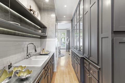 An elegant galley kitchen with gray cabinetry, hardwood floors, and open shelving adorned with decorative plates.