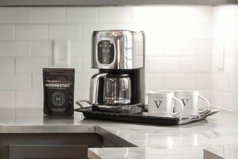 A modern coffee station featuring a sleek coffee maker, a bag of Minnestay coffee, and two white mugs on a tray.