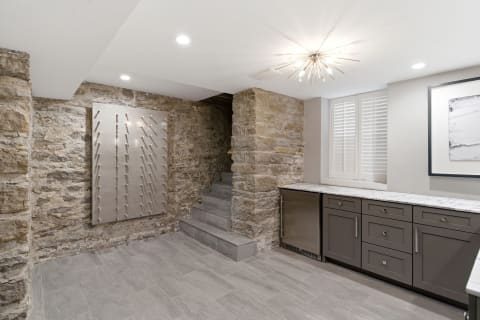 An entertainment space with rustic stone walls, modern sleek cabinets, and a unique metallic art piece.