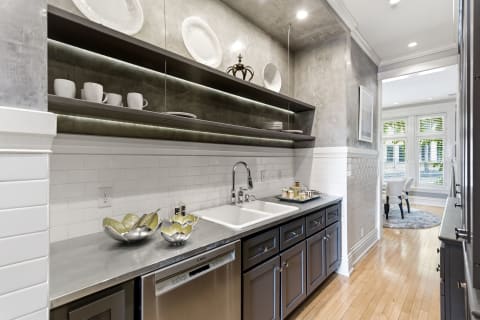 Modern kitchen with gray cabinetry, open shelves, and a double-basin sink, showcasing elegant tableware and natural light.