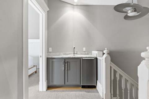 Elegant upstairs wet bar featuring granite countertops and gray cabinetry with a mini fridge.