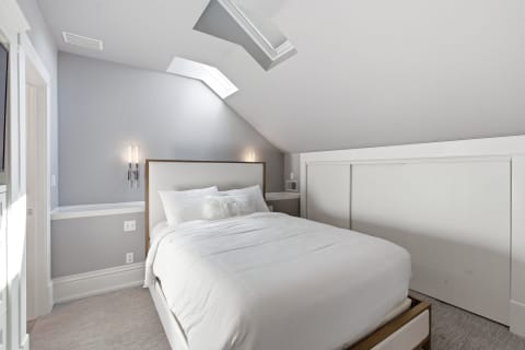 A serene bedroom with gray walls, a skylight, and white bedding.