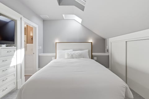 A serene bedroom showcasing a white bed, soft linens, and ambient light against grey walls.
