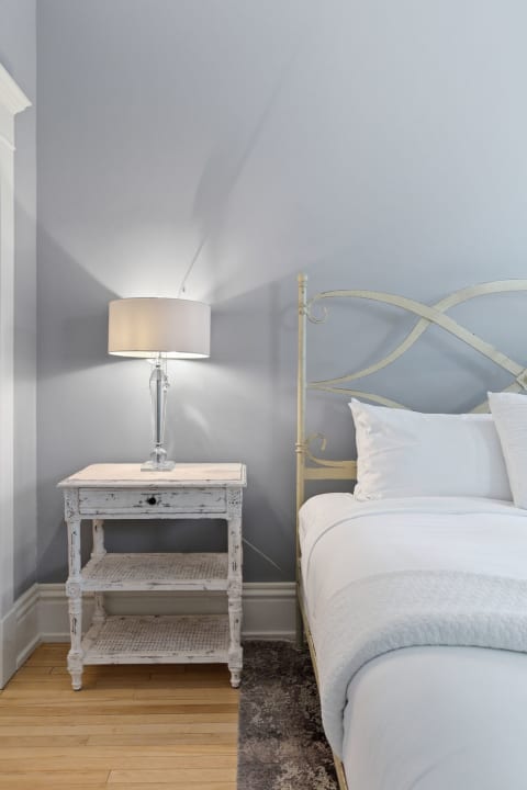 A serene bedroom with pale blue walls, vintage yellow bed frame, white linens, and a rustic bedside table with a lamp.