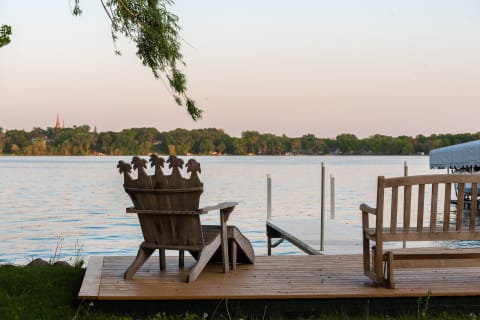 Lakeside view featuring a decorative wooden chair and bench on a deck.